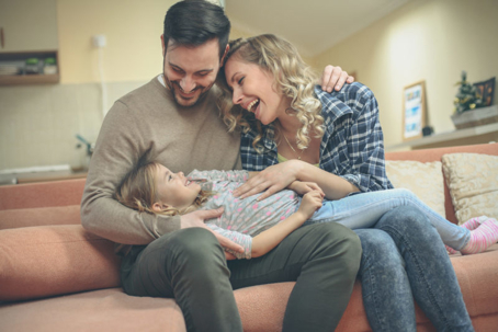 A smiling family sits together on a couch.