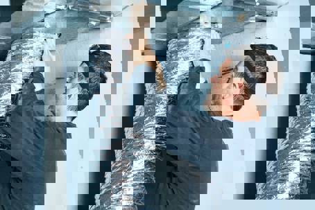 A service technician connects a flexible duct to a ceiling vent
