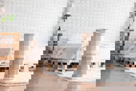 A modern white air purifier sits on a shag rug in a minimalist bedroom setting