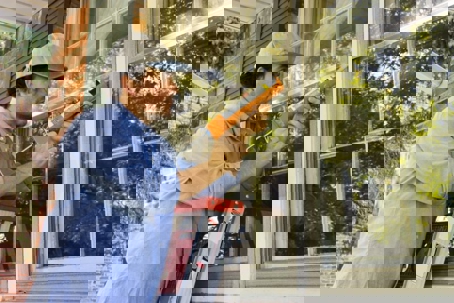 A man on a ladder caulks the trim around a window.