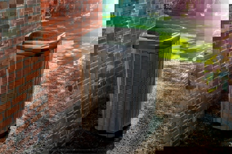 Outdoor AC unit, positioned outside a brick house on a patch of gravel