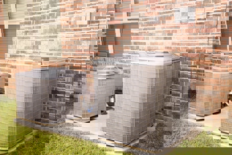 Two air conditioning units sit outside a brick building on a concrete slab, highlighting the importance of HVAC maintenance.