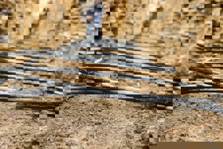 Black pipes run horizontally in a trench in the ground.