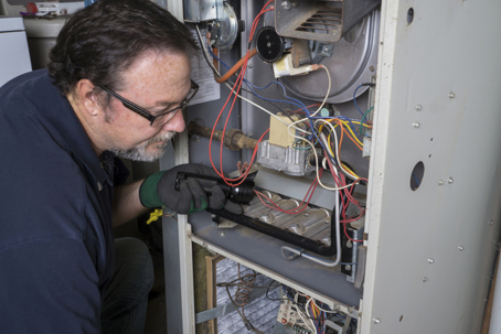 An HVAC technician inspects a furnace with a flashlight, ensuring a safe and functional appliance.