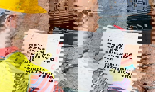 An HVAC technician is holding a sign that spells out "Heating, Ventilating, Air Conditioning".