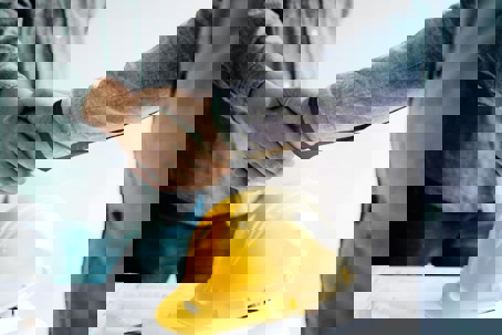 A close up photo shows two construction workers shaking hands, a yellow construction hat sits below.