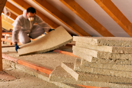 A person in protective gear insulates an attic with fiberglass, improving home energy efficiency.