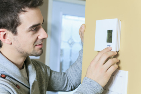 A man adjusts the thermostat on a wall.