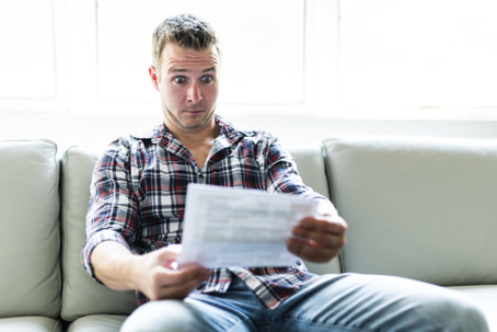 A man sits on a couch with a shocked expression