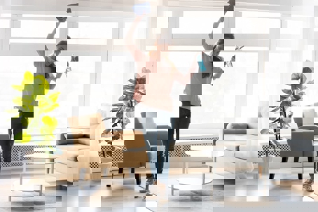 A woman cleans her home with vigor, holding a spray bottle and cloth with arms raised.