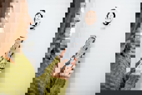 Person controls smart thermostat with smartphone.