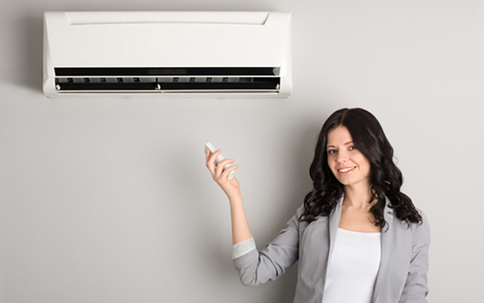 A smiling woman adjusts her air conditioner with a remote
