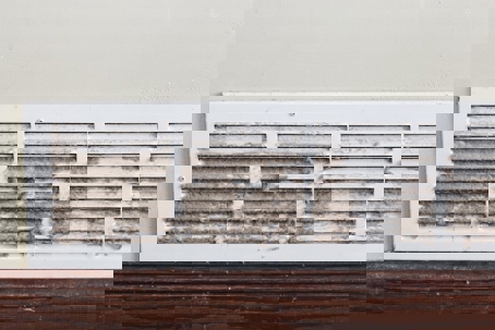 A close-up of a dirty white air vent, emphasizing the need for regular duct cleaning.